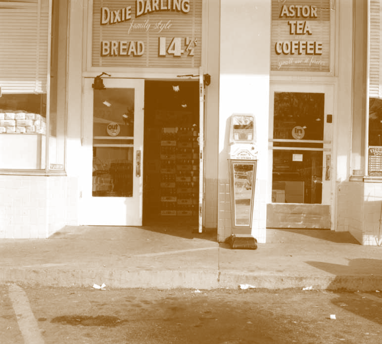 The front windows of this Winn-Dixie Food Store are adorned with handpainted advertisements. The ads shown include one for for Dixie Darling family style bread on sale for 14.5 cents and an ad for Astor Tea and Coffee.max-width:100%; max-height:100%;